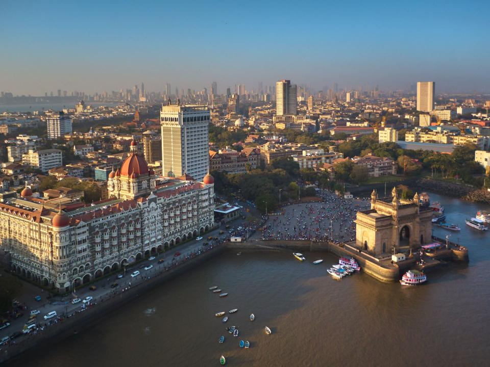 Luftaufnahme von Mumbai mit dem Gateway of India und dem Taj Mahal Palace Hotel am Ufer, umgeben von der geschäftigen Stadt____