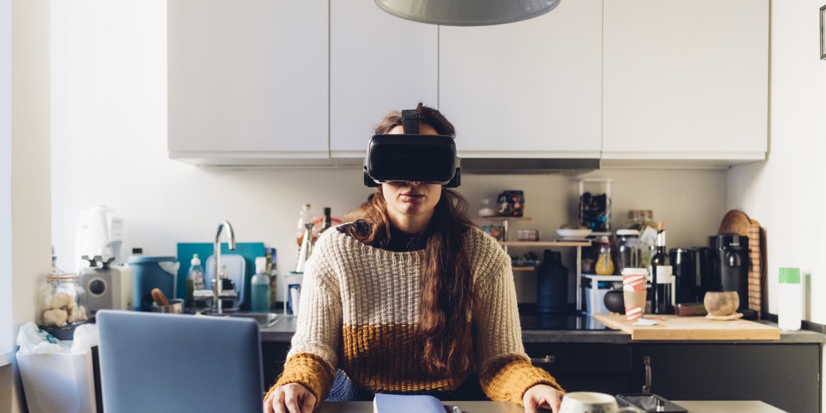 Frau sitzt vor ihrem Laptop und trägt eine VR-Brille.