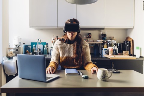 Frau sitzt vor ihrem Laptop und trägt eine VR-Brille.