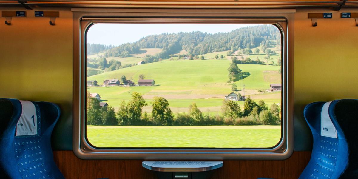Blick aus einem Zugfenster in eine malerische, grüne Landschaft
