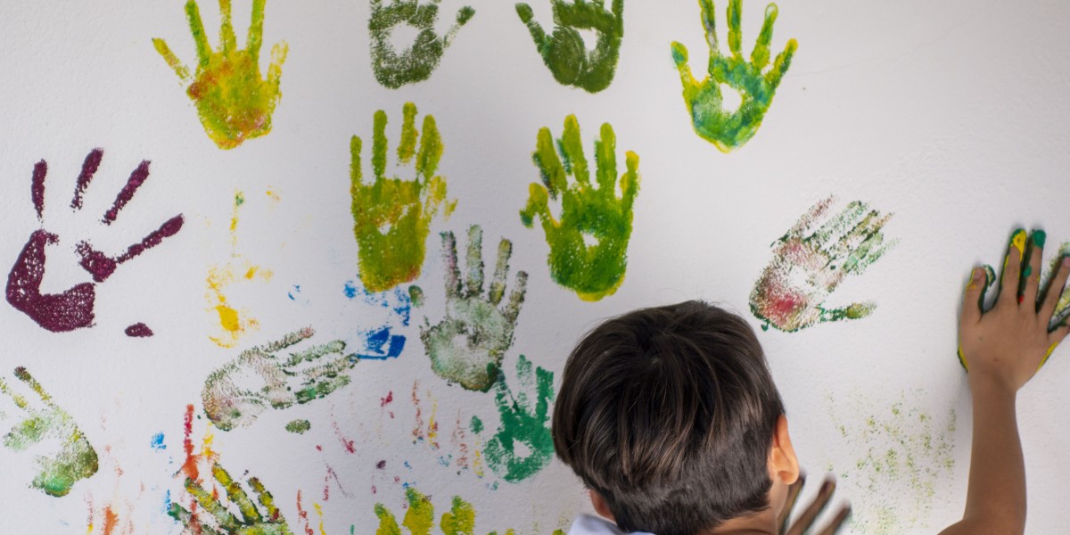 Ein Junge drückt seinen bunten Handabdruck auf eine Wand voller weiterer Handabdrücke.