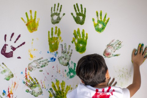 Ein Junge drückt seinen bunten Handabdruck auf eine Wand voller weiterer Handabdrücke.