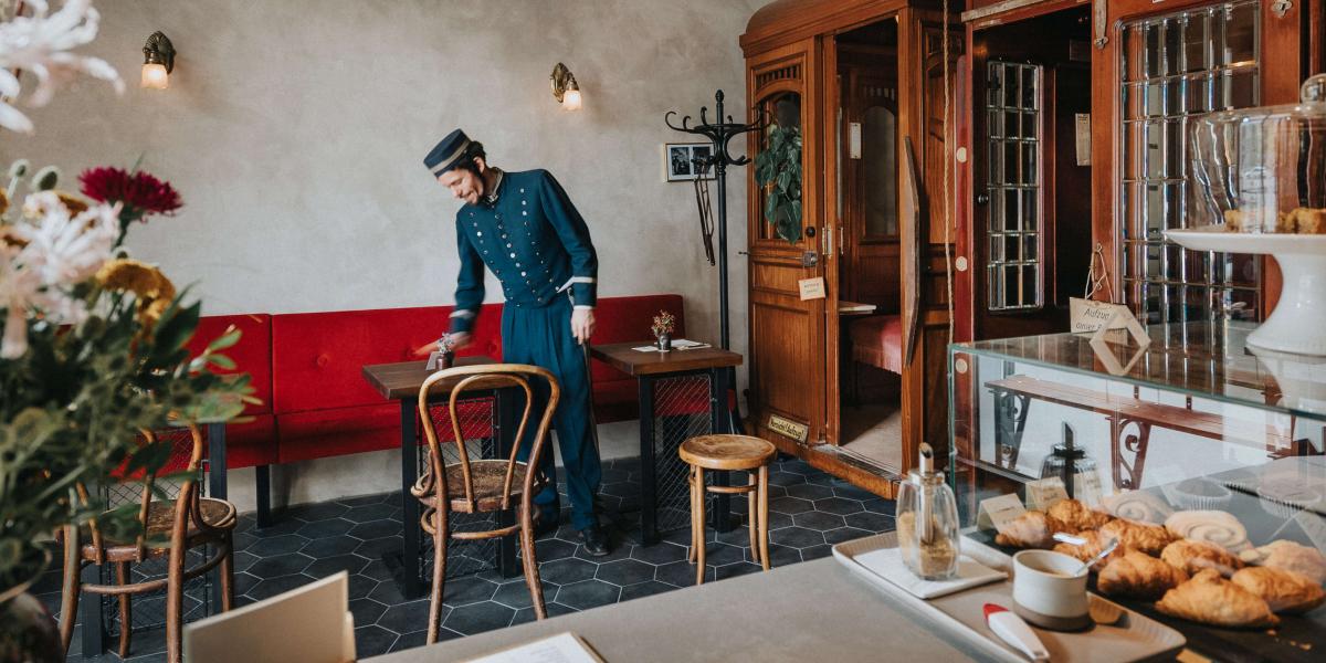 Kellner in historischer Uniform räumt Tisch in einem gemütlichen Café mit klassischem Interieur auf.