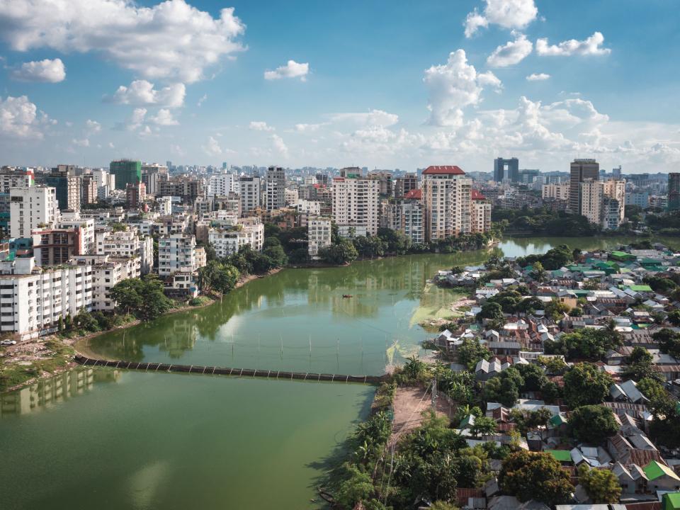 Luftaufnahme von Dhaka mit einem grünen See, umgeben von modernen Hochhäusern und dicht besiedelten Wohngebieten____