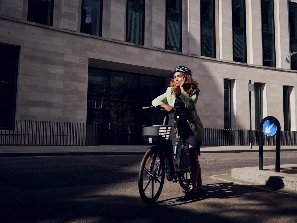 Frau in grüner Jacke fährt E-Bike in städtischer Umgebung.____