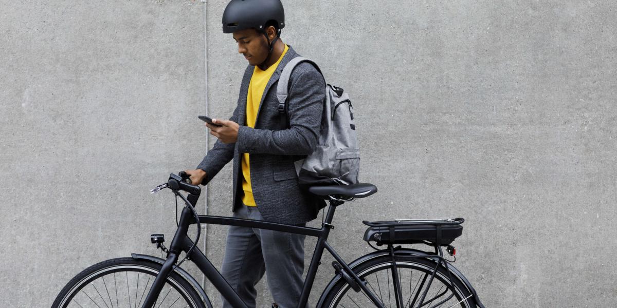 ann in gelbem Pullover überprüft Smartphone neben schwarzem E-Bike.