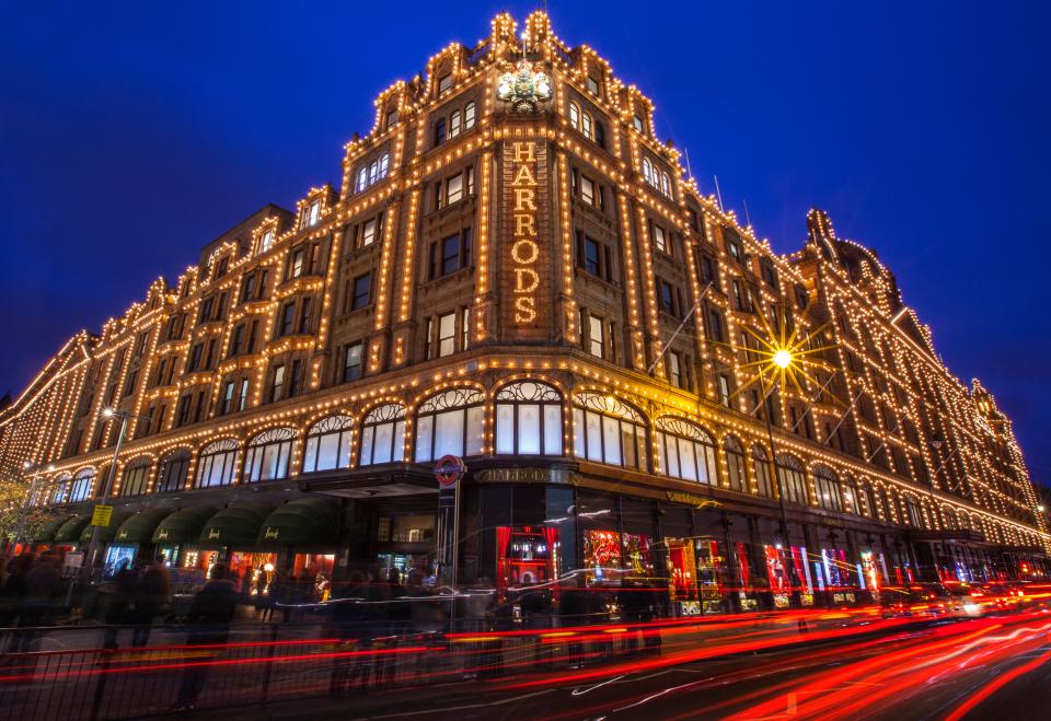 Beleuchtetes Harrods-Kaufhaus in London bei Nacht mit Lichtspuren vorbeifahrender Autos____