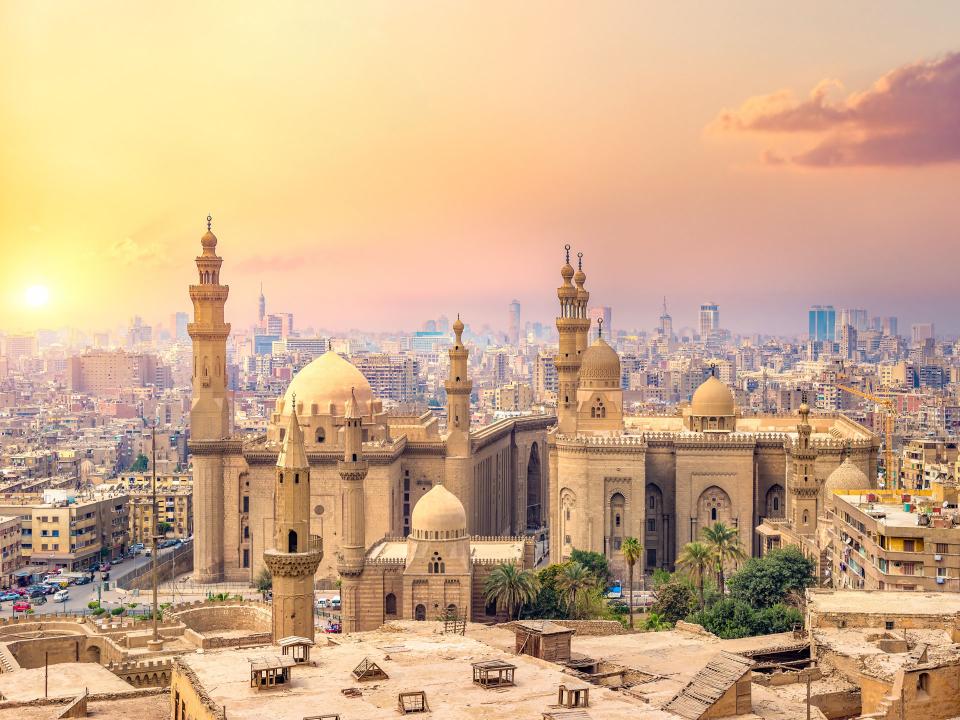 Luftaufnahme von Kairo bei Sonnenuntergang, mit der historischen Sultan-Hasan-Moschee im Vordergrund und der modernen Stadtlandschaft im Hintergrund____