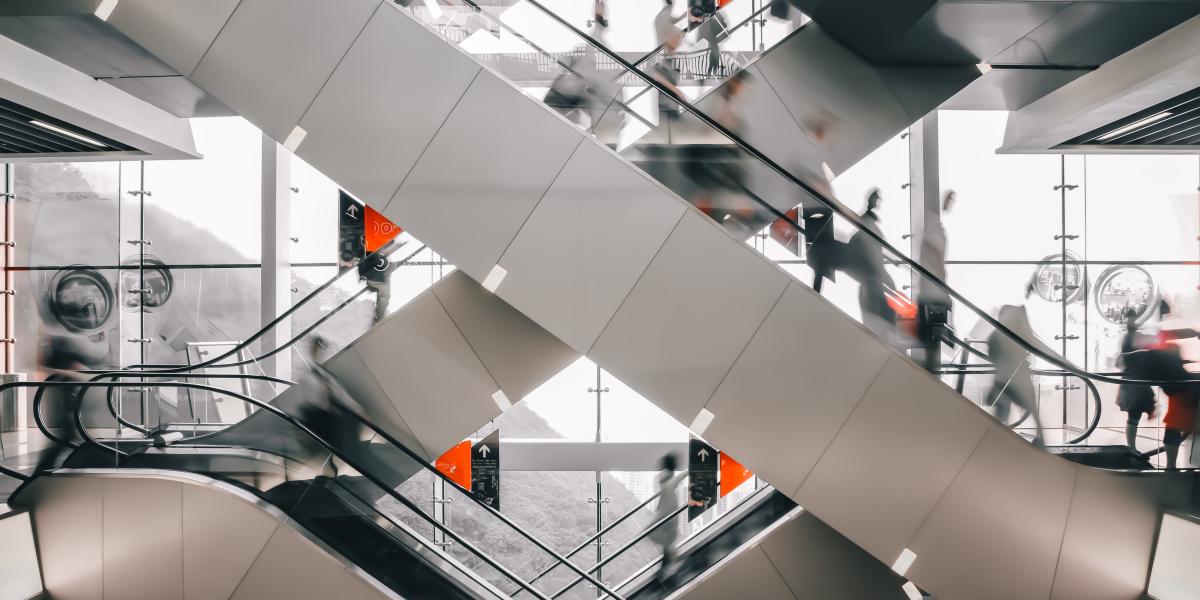Kreuzende moderne Rolltreppen in einem lichtdurchfluteten Einkaufszentrum mit vielen Personen in Bewegung