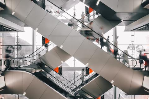 Kreuzende moderne Rolltreppen in einem lichtdurchfluteten Einkaufszentrum mit vielen Personen in Bewegung
