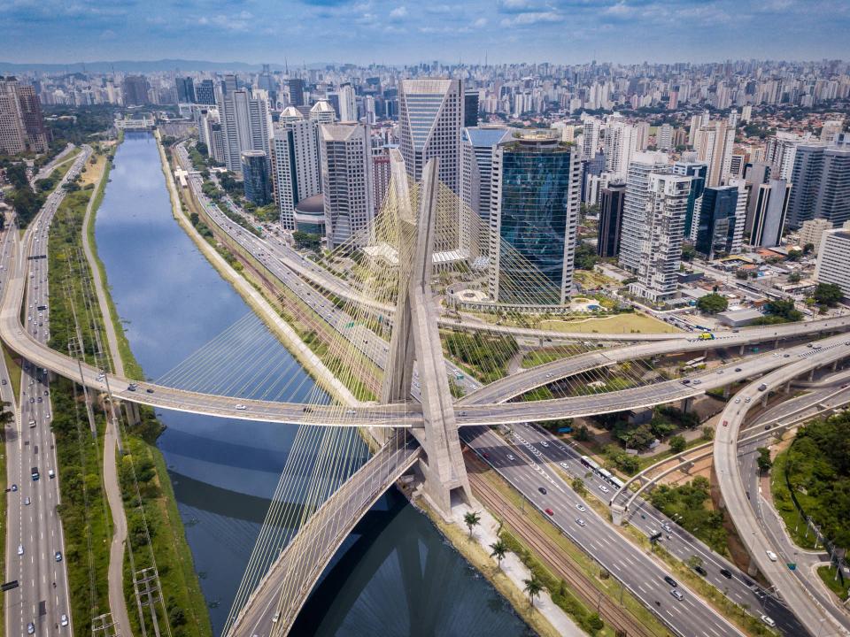 Luftaufnahme der Brücke "Ponte Estaiada Octávio Frias de Oliveira" in São Paulo, umgeben von modernen Hochhäusern und Autobahnen entlang eines Flusses____