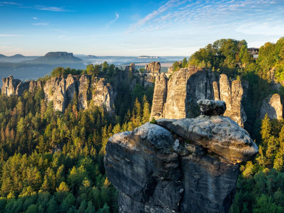 Steile Felsen ragen aus einem Meer aus Bäumen empor, eine Brücke verbindet einige davon miteinander.____