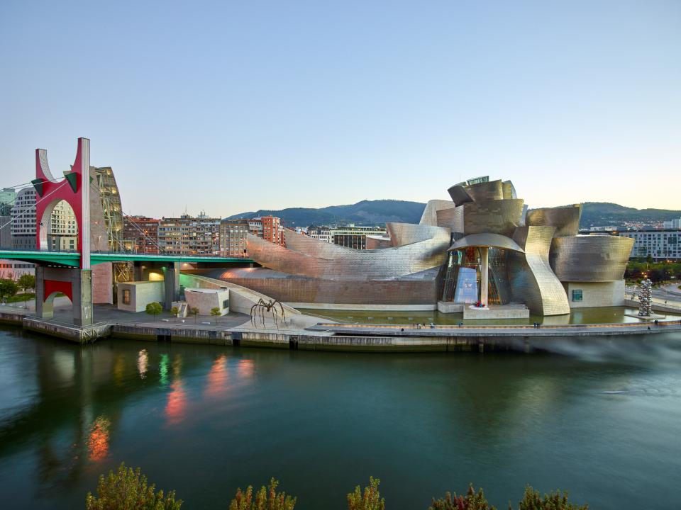 Guggenheim-Museum in Bilbao mit geschwungenen Titanfassaden am Flussufer bei sanfter Abendbeleuchtung.____