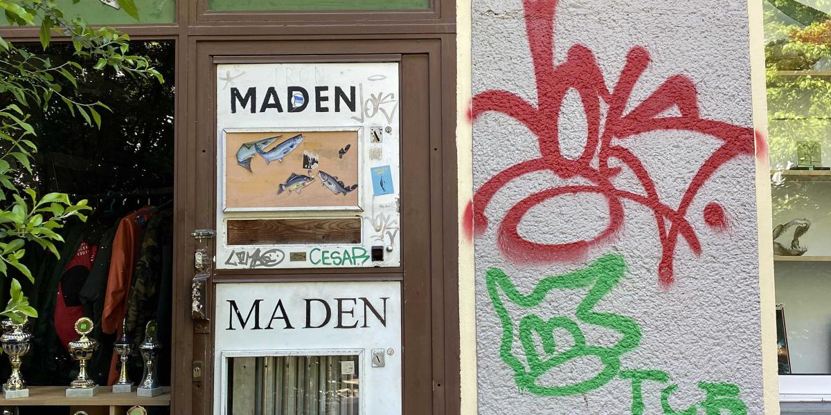 Automat mit der Aufschrift "Maden" und einem Fensterausschnitt, der Fische zeigt, an einer Graffiti-beschmierten Wand