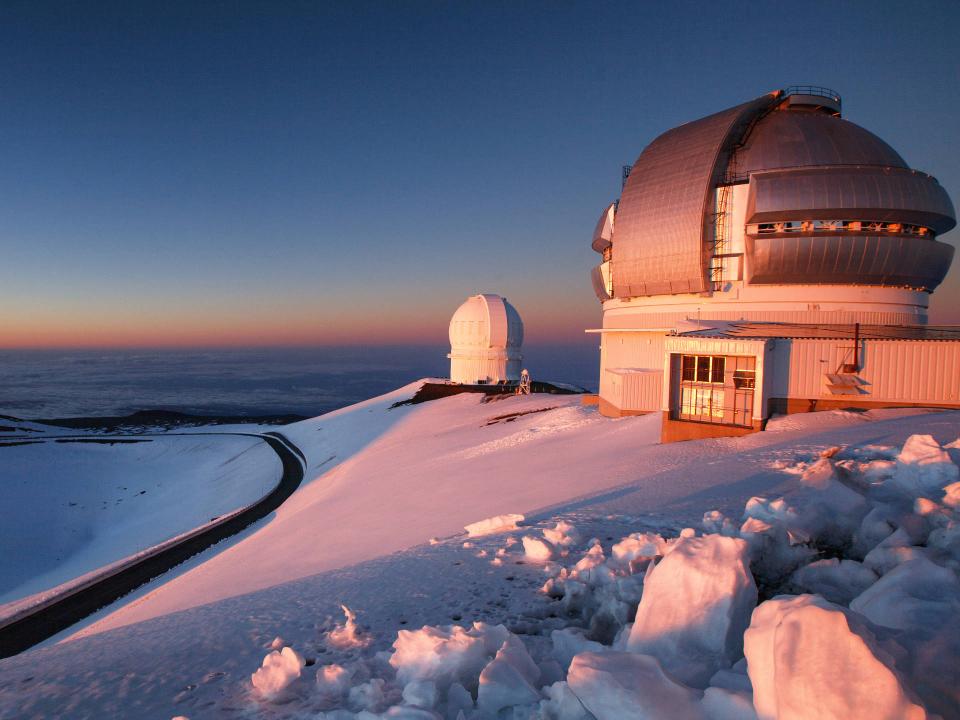 Schneebedeckte Observatoriumskuppeln bei Sonnenuntergang, auf einem Berg mit klarem Himmel und kurvigen Straßen____