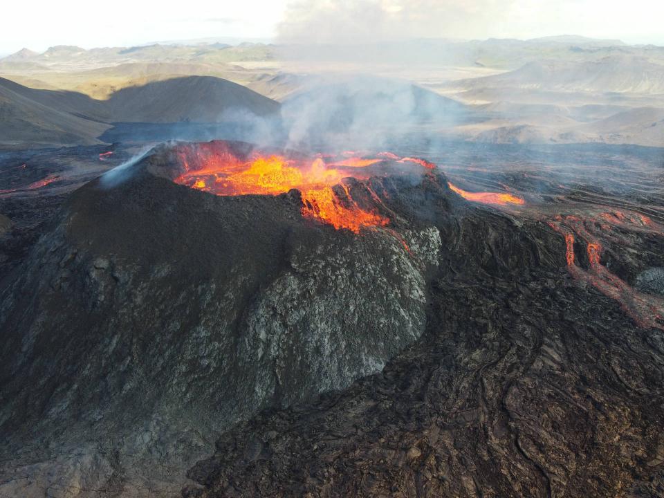 Lavafeld eines ausbrechenden Vulkans, glühend in feurigem Orange, das sich über das dunkle felsige Gelände erstreckt____