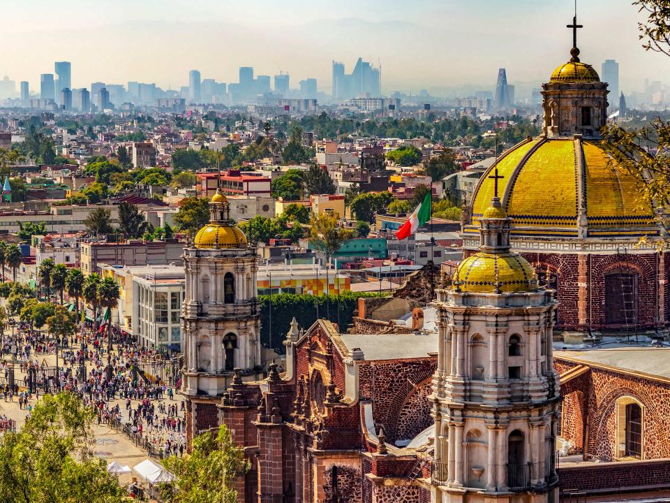 Luftaufnahme der Basilika von Guadalupe in Mexiko-Stadt, mit ihren goldenen Kuppeln und der Skyline im Hintergrund____