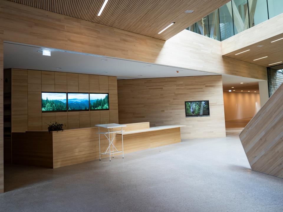 Holzverkleideter Innenraum mit Empfangstresen und digitalen Bildschirmen, die Naturansichten zeigen.____