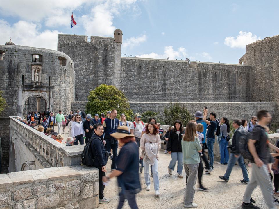 Touristenmassen auf Brücke vor der Altstadt von Dubrovnik, Steinmauer und kroatische Flagge im Hintergrund.____