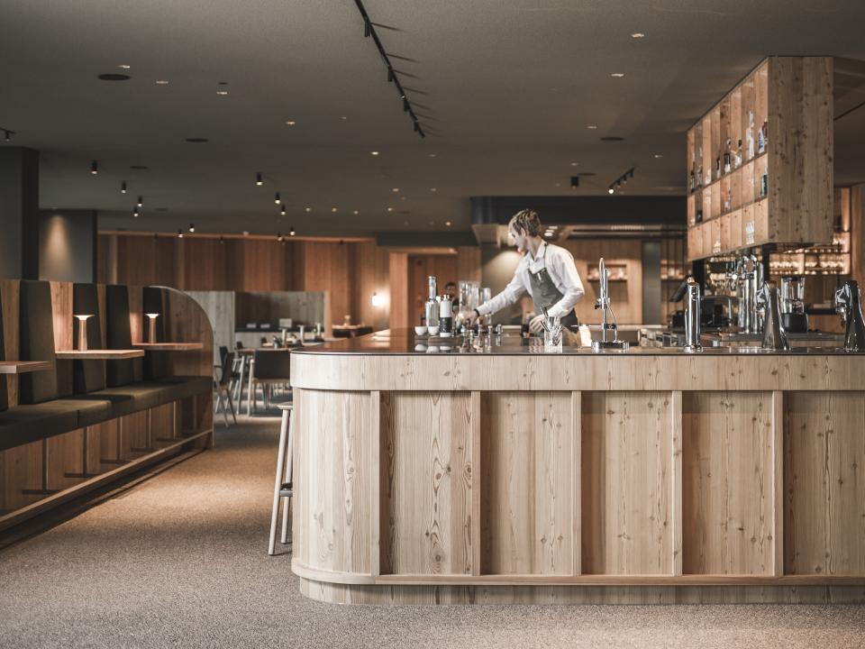 Moderne Hotelbar mit Holztresen, Barkeeper bereitet Getränke zu, gemütliche Sitzbereiche.____