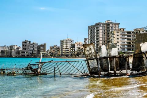 eilweise im türkisfarbenen Meer versunkener Zaun, dahinter eine Reihe verfallener Küstengebäude