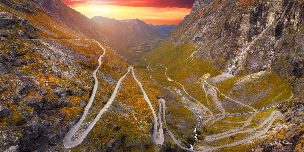 Kurvenreiche Passstraße windet sich durch felsige Berglandschaft im Sonnenuntergang mit dramatischem Himmel