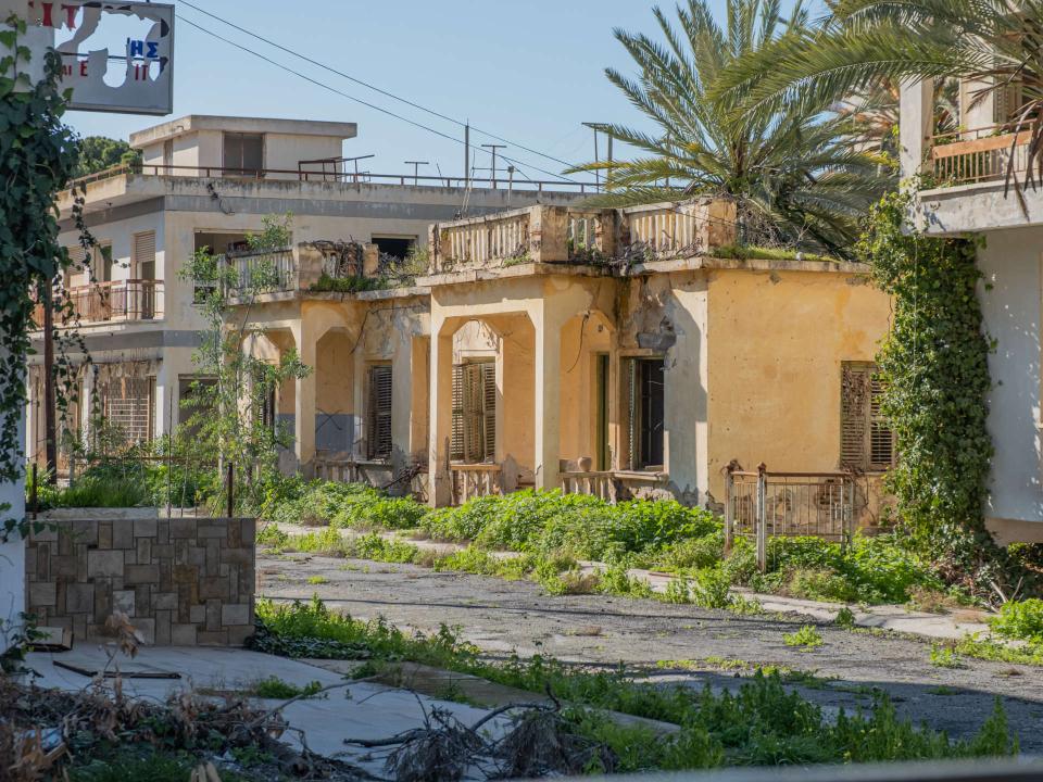 Nahaufnahme von verlassenen, verfallenen Häusern mit überwucherten Balkonen und einer Palme____