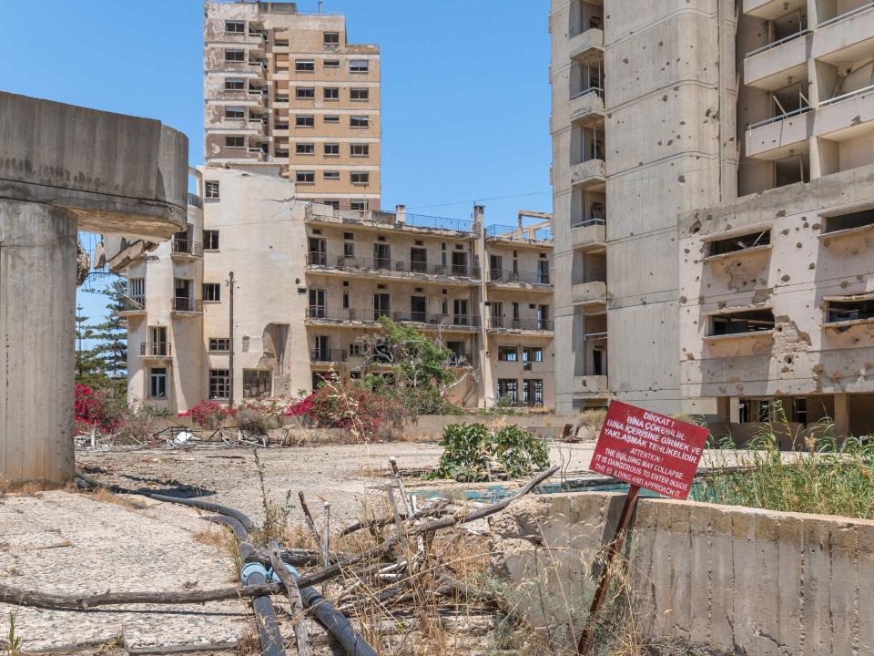 Verfallene Betongebäude mit Trümmern und einem Warnschild: 'DANGER! Building is in danger to collapse.'____