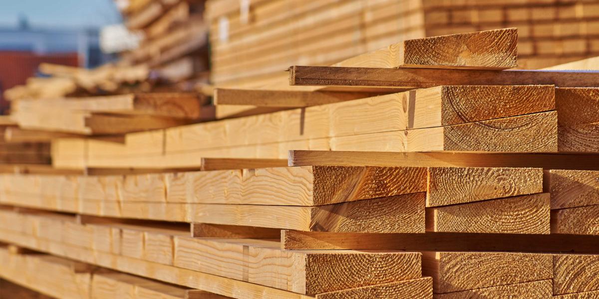 Gestapelte, glatt gehobelte Holzbretter aus hellem Nadelholz auf einem Holzlagerplatz bei Tageslicht