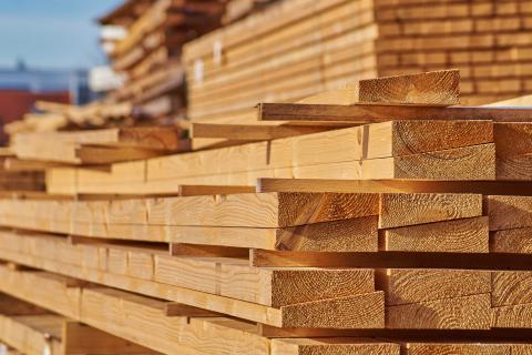 Gestapelte, glatt gehobelte Holzbretter aus hellem Nadelholz auf einem Holzlagerplatz bei Tageslicht