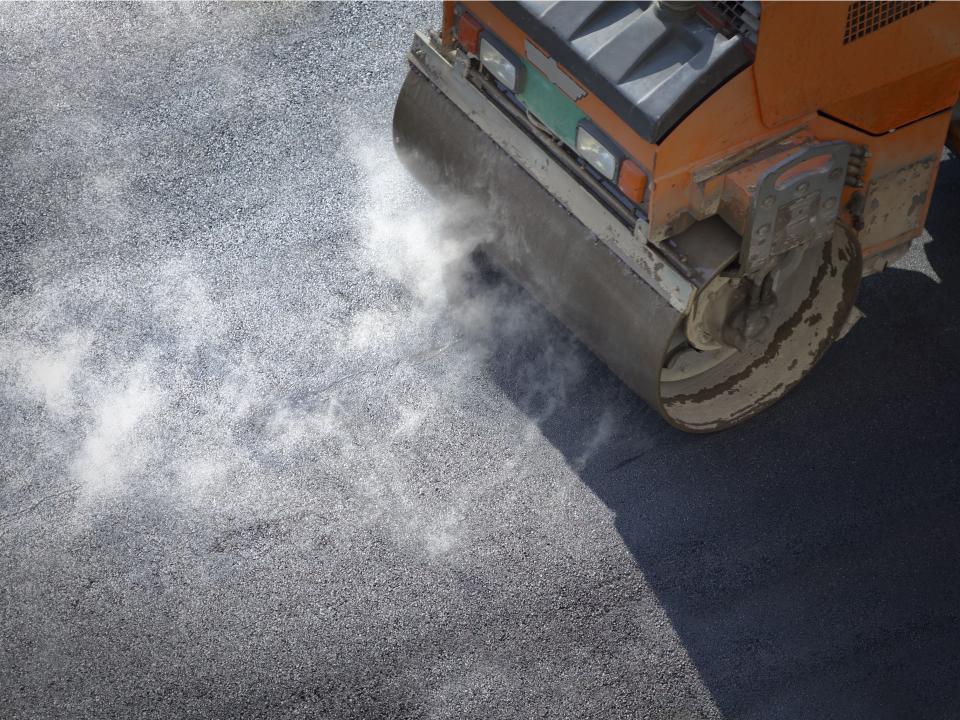 Dampfende Straßenwalze verdichtet frisch gelegten Asphalt.____