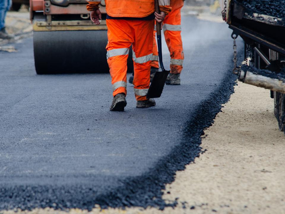 Arbeiter in orangenen Hosen bereiten Asphalt auf der Straße vor.____