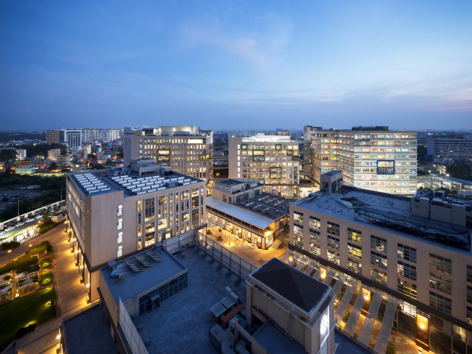 Panoramablick auf moderne Bürogebäude bei Dämmerung, beleuchtete Fenster und Straßen in einer städtischen Umgebung.____