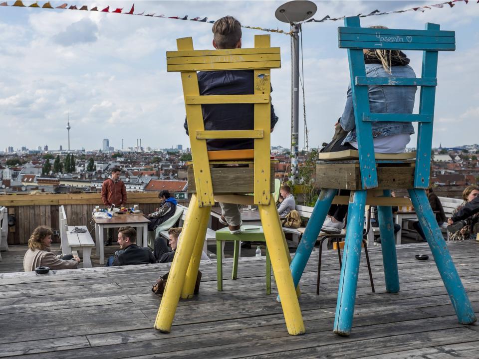 Zwei Personen sitzen auf großen Stühlen mit Blick auf Berlins Skyline.____