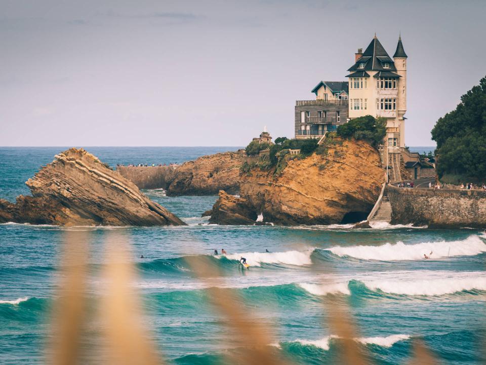 Einzelner Surfer nimmt Welle vor steilen Felsklippen mit schlossartigem Aussichtspunkt über dem Meer____