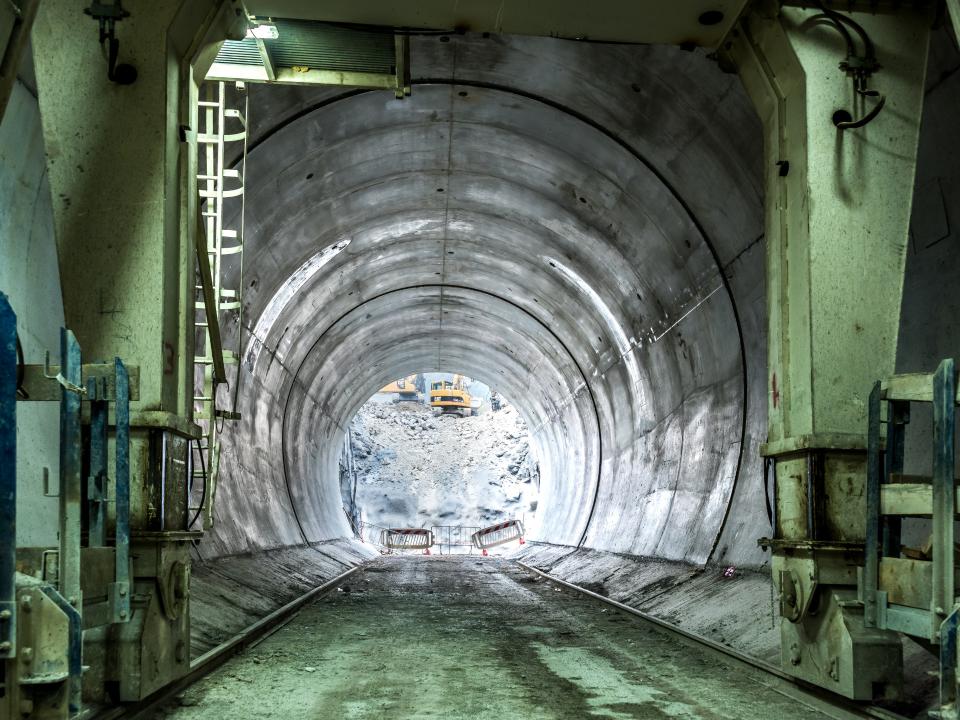 Blick in einen halbfertigen Tunnel mit Betonwänden und Baustellenausrüstung im Hintergrund.____