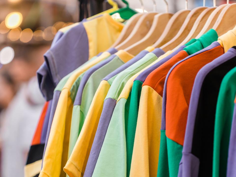 Bunte T-Shirts auf Holzbügeln in einer Kleiderstange.____