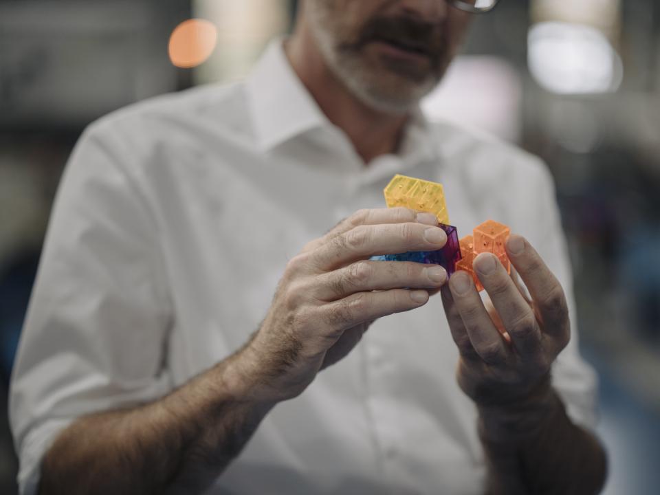 Mann in weißem Hemd hält farbige, geometrische Spielsteine.____