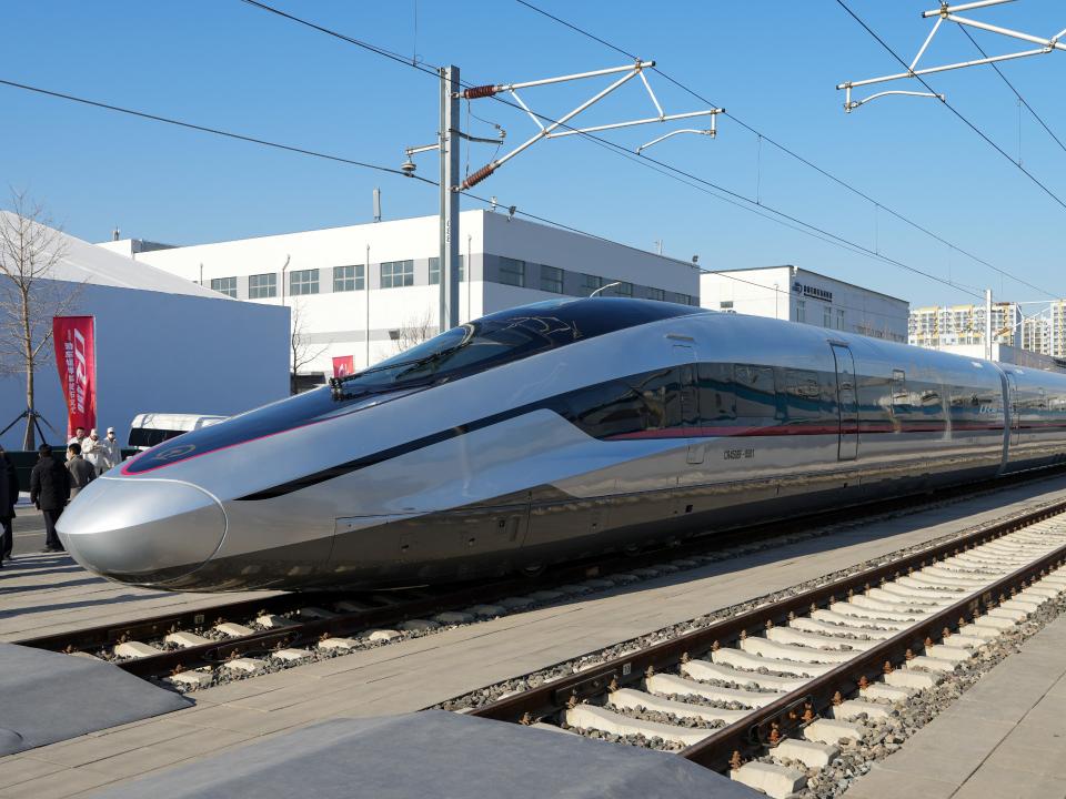 Hochgeschwindigkeitszug mit futuristischem Design auf Schienen vor einem modernen Bahngelände____