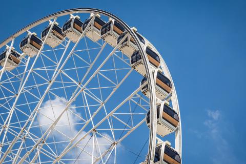 Detailaufnahme eines Riesenrads mit geschlossenen Gondeln vor blauem Himmel.