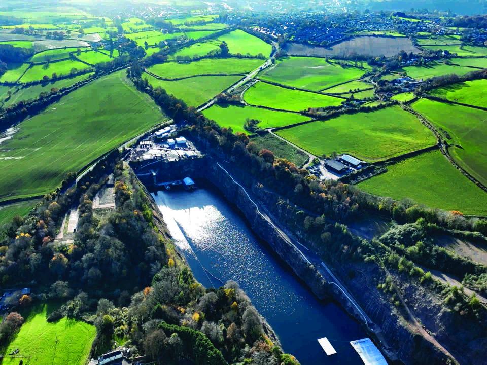 Luftaufnahme eines Steinbruchs mit Wasserbecken, umgeben von grünen Feldern und kleinen Gebäuden im Tageslicht____