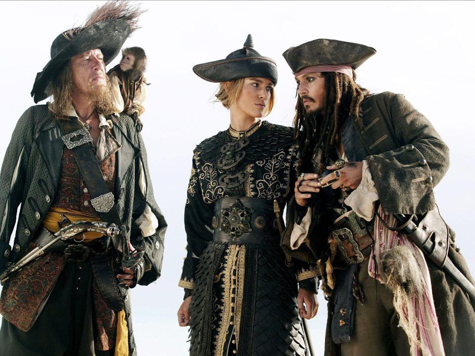 Drei Piraten in aufwendigen Kostümen stehen zusammen, ein Affe auf der Schulter eines Mannes.____