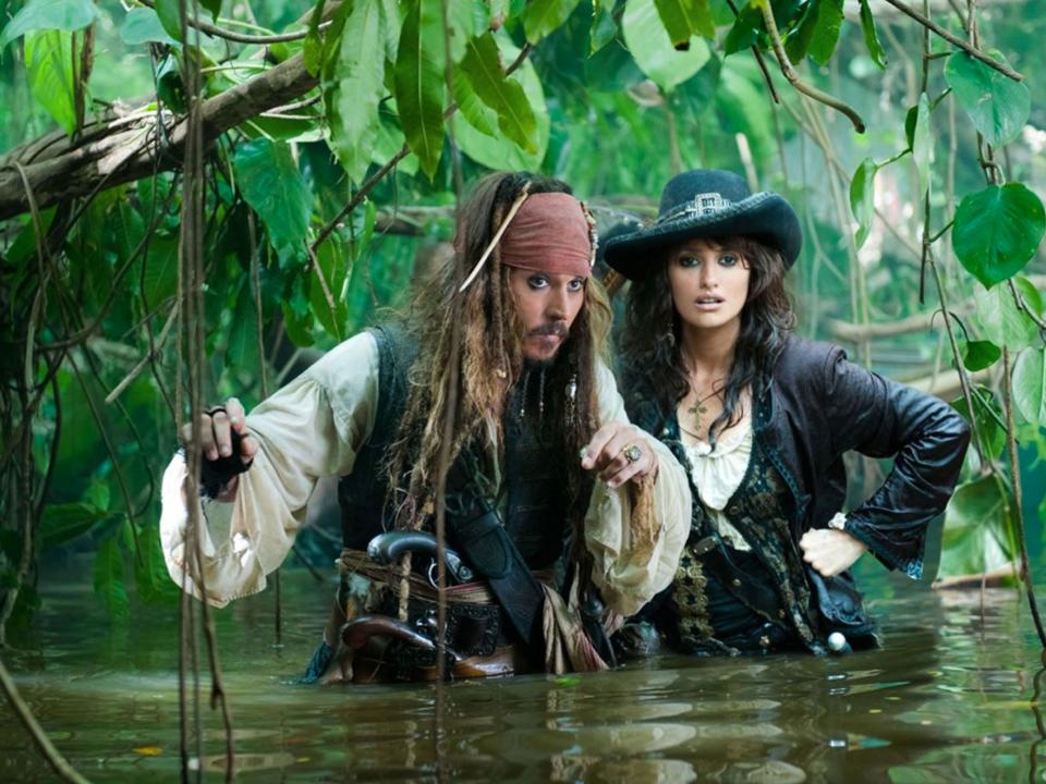 Zwei Piraten in aufwendiger Kleidung waten durch dicht bewachsenen Dschungel-Sumpf.____