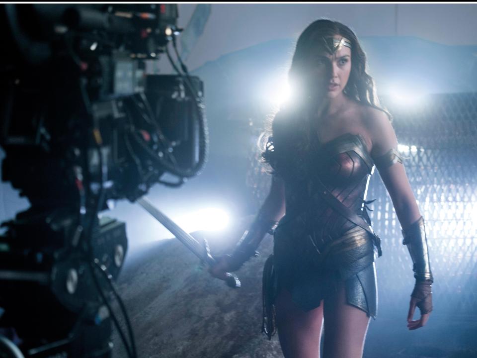 Frau in Rüstung mit Schwert vor Filmkamera, leuchtende Lichter im Hintergrund.____