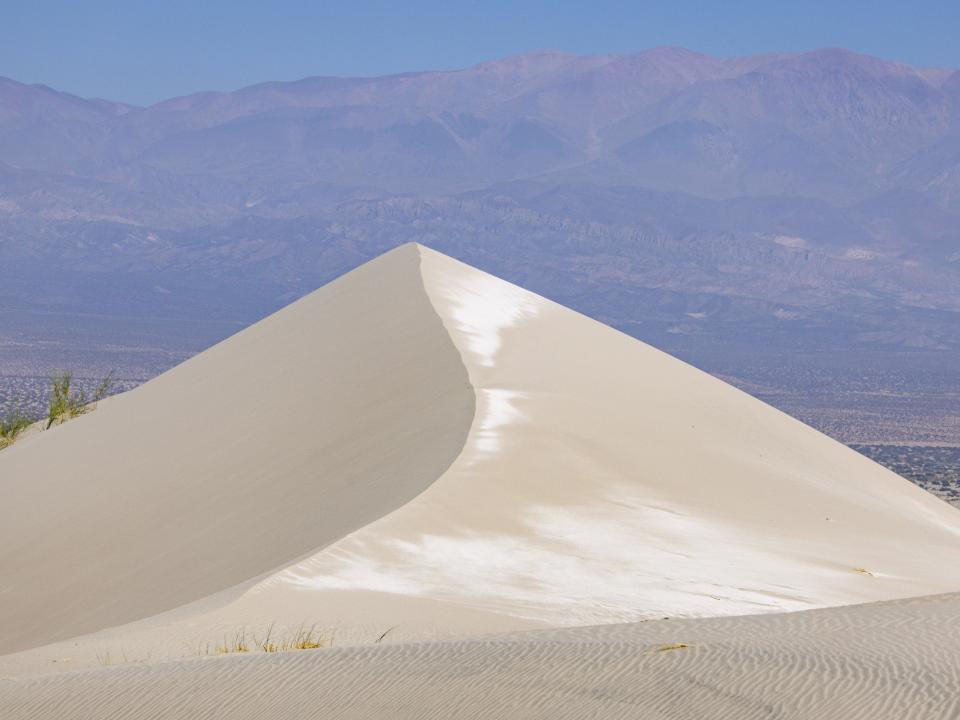 Hohe Sanddüne mit scharfer Kante und Bergen im Hintergrund bei klarem Himmel.____