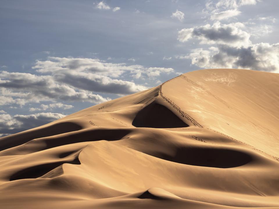 Sanddüne bei tiefstehender Sonne mit Wolken im Himmel und Fußspuren auf der Düne.____