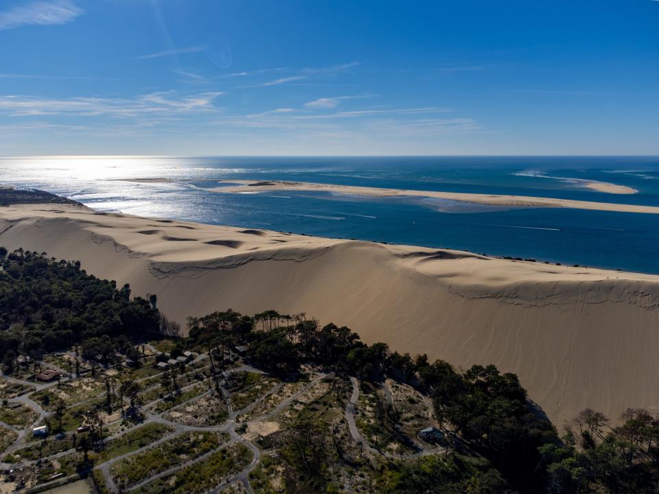Große Sanddüne an der Küste mit Meer im Hintergrund und einem Campingplatz am Rand.____