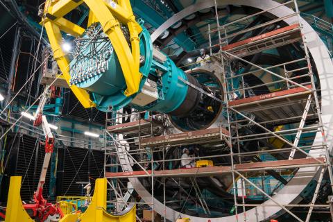 Techniker arbeiten an einem riesigen astronomischen Gerät mit komplexen Metallstrukturen