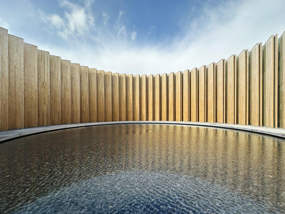 Runde Holzwand um ruhigen Wasserbereich, klare, moderne Architektur.____