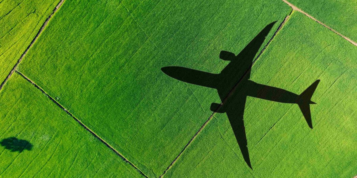 Schatten eines großen Flugzeugs über grünen Feldern, die weite Ackerlandschaften und landwirtschaftliche Flächen zeigen